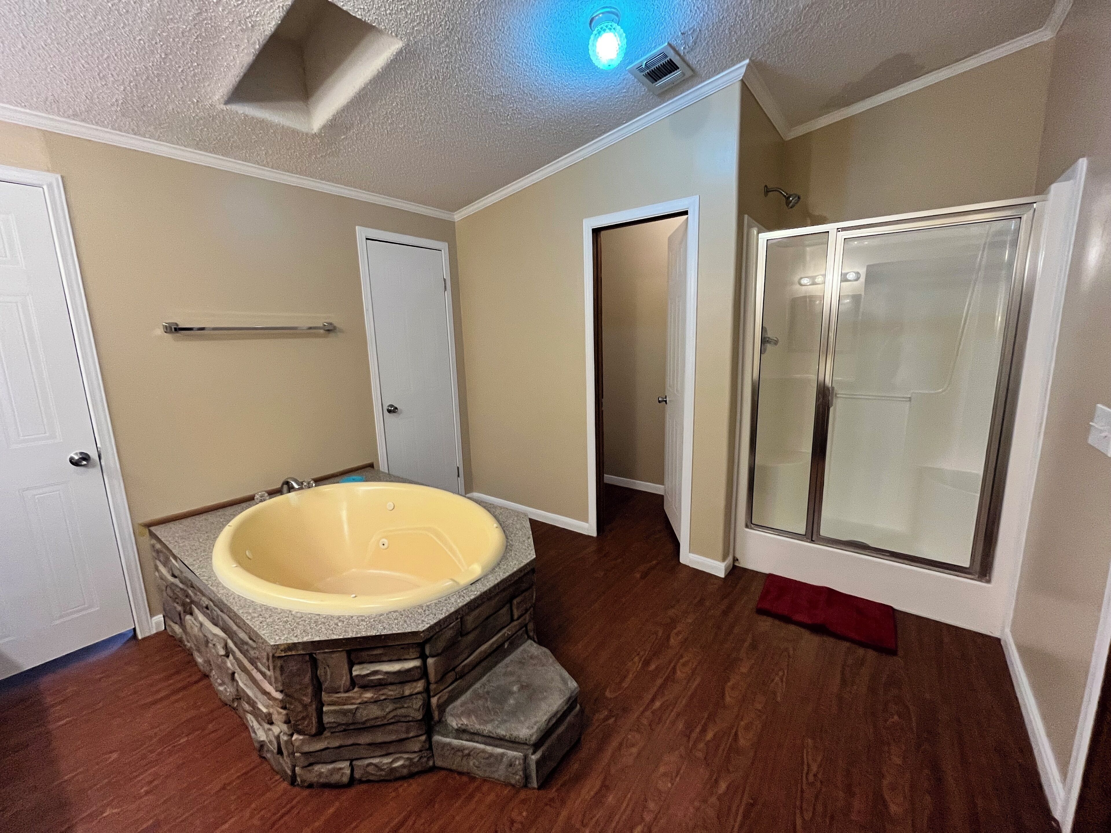 Ein Badezimmer mit einer Steinbadewanne, einer Duschkabine aus Glas und Holzboden.