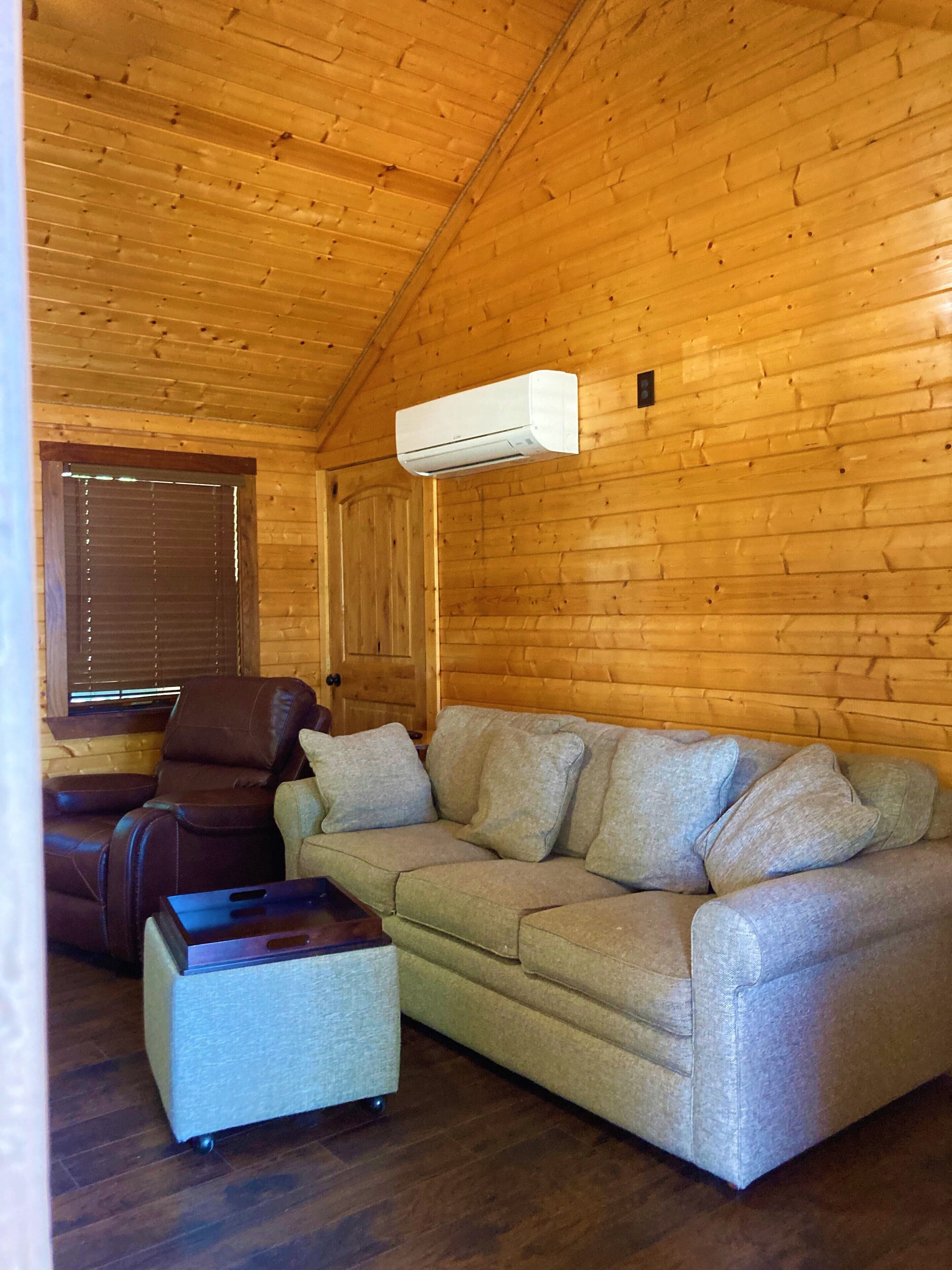 A wooden cabin interior with a sofa, a recliner, and a small table.