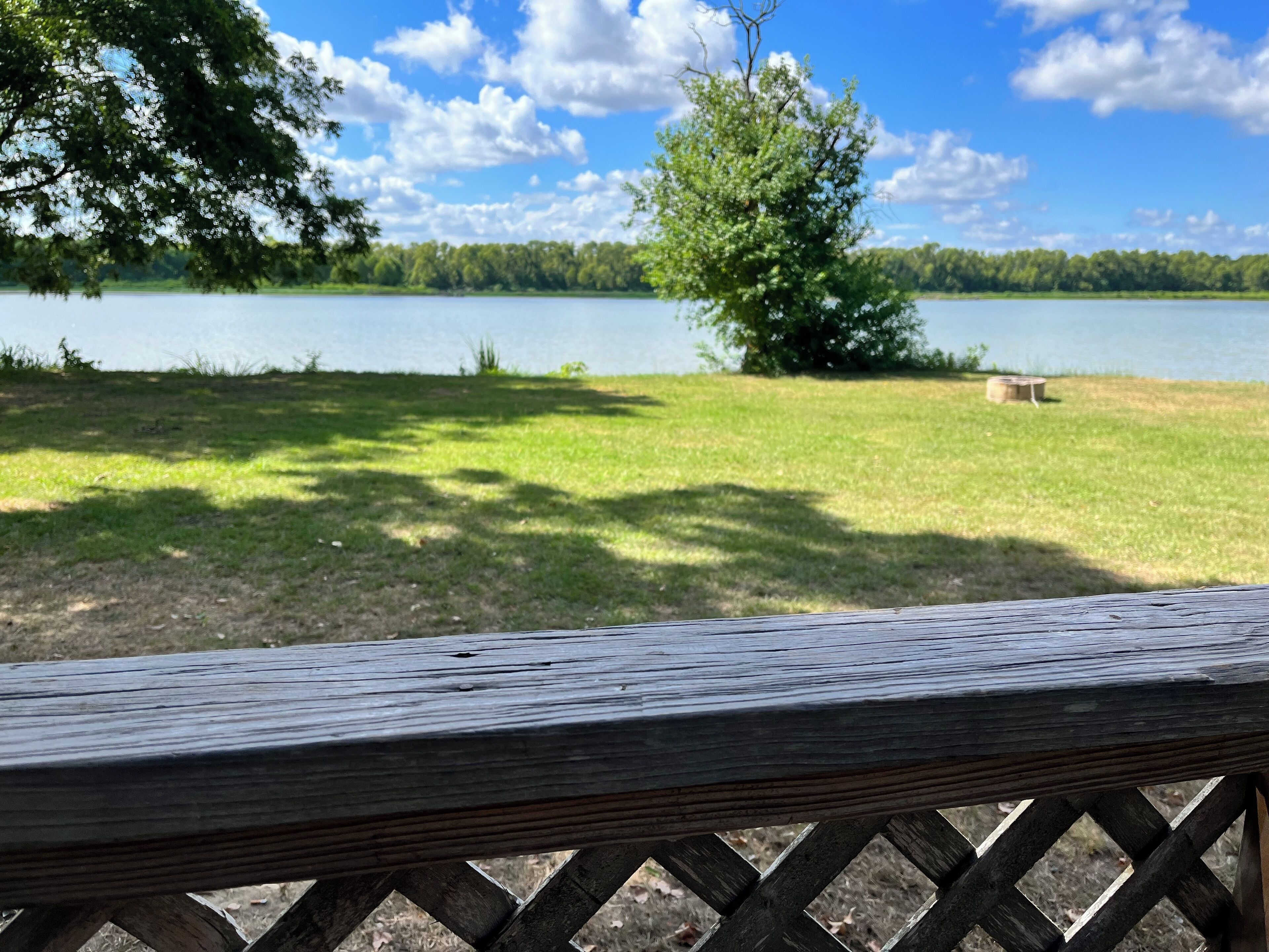 A wooden bench overlooking a lake with a grassy area and trees in the background.