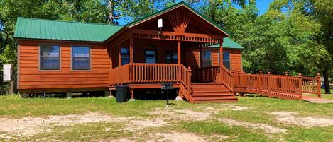 A wooden cabin with a green roof, a porch, and a staircase leading to the entrance.