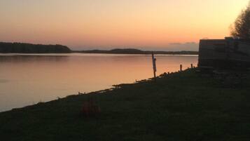 Un lac paisible au coucher du soleil, avec une aire de camping et une caravane sur la droite.