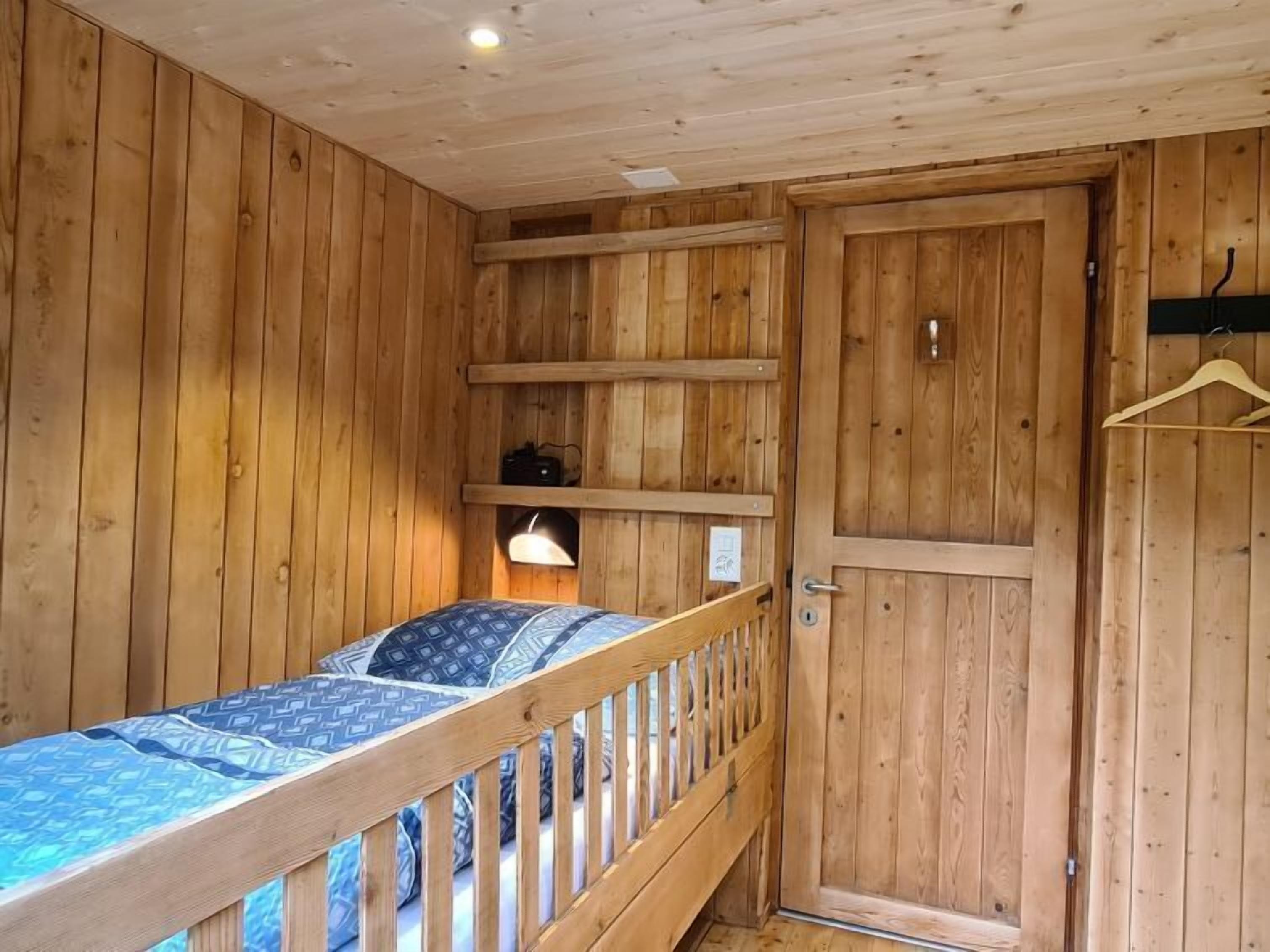 A wooden cabin room with a bunk bed, a door, and a shelf with a lamp.
