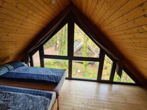 Une chambre dotée d’une grande fenêtre, d’un plafond en bois et d’un lit avec une literie à motifs.
