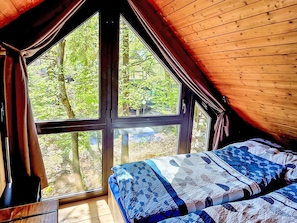 A room with a large window, a bed with a patterned bedspread, and wooden walls.
