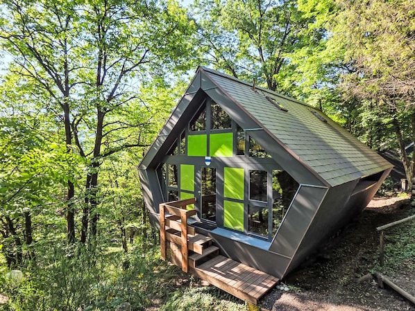 A small, modern cabin with a sloped roof, large windows, and a wooden staircase leading to the entrance.