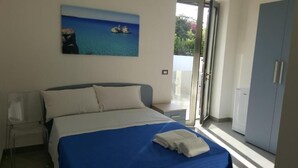 A bedroom with a bed, a painting of a beach scene, a wardrobe, and a sliding door to a balcony. - Acquamarina (Melendugno)
