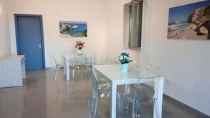 A modern dining area with a glass table and chairs, a blue door, and two paintings on the walls. - Acquamarina (Melendugno)