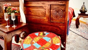 Un letto in legno con una coperta dai colori vivaci, un comodino con un vaso di fiori e una lampada.