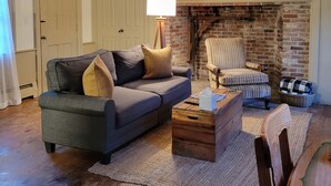 Un salon chaleureux avec un canapé d’angle, une table basse en bois et une cheminée en briques.