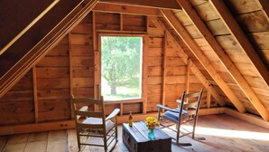 Une pièce mansardée en bois, avec deux fauteuils à bascule, une petite table sur laquelle est posé un vase de fleurs et une fenêtre donnant sur les arbres.