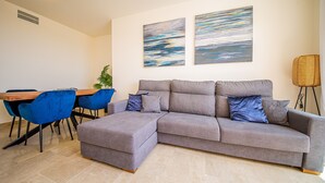 Uma sala de estar moderna com um sofá seccional cinza, cadeiras azuis, uma mesa de jantar de madeira e duas pinturas abstratas na parede.