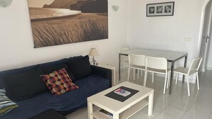 Una sala de estar con un sofá, una mesa de centro, una mesa de comedor con sillas y un cuadro en la pared.