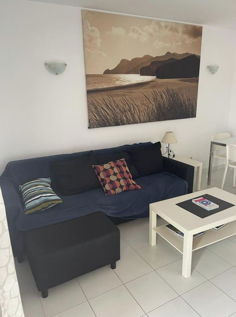 Een woonkamer met een donkerblauwe bank, een passende voetenbankje, een witte salontafel met een tijdschrift en een schilderij van een landschap aan de muur.
