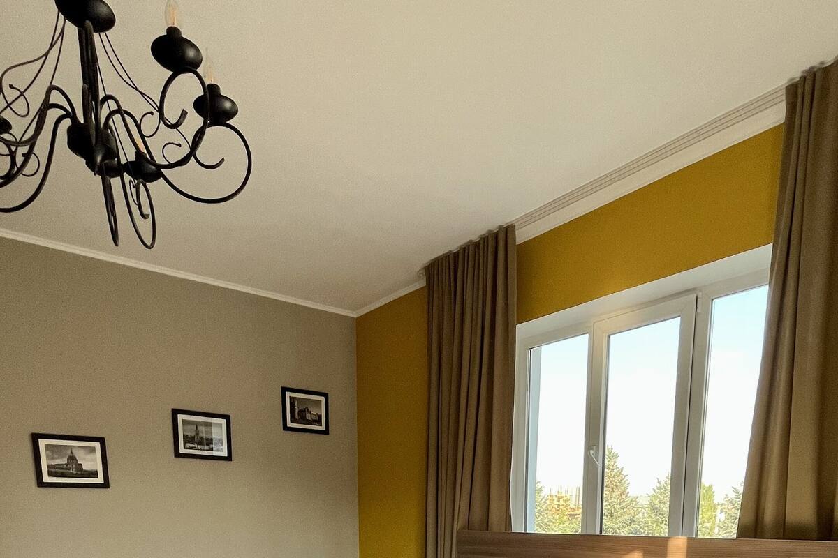 Une chambre d’hôtel avec un grand lit, deux petits lits, un plancher en bois, un lustre et une fenêtre avec des rideaux.