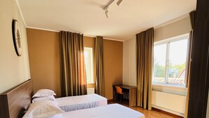 A hotel room with two beds, a desk, and a view of the outdoors.