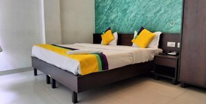 Una cama bien hecha con colcha blanca y amarilla, dos almohadas y una mesita de noche con un teléfono y una lámpara.