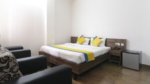 Habitación de hotel con cama, mesita de noche, silla y un refrigerador pequeño.
