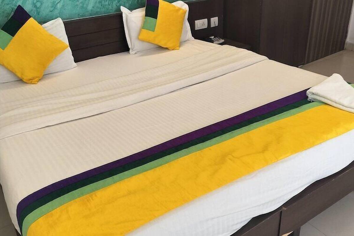 A neatly made bed with a white mattress and a colorful blanket featuring yellow, green, and purple stripes.