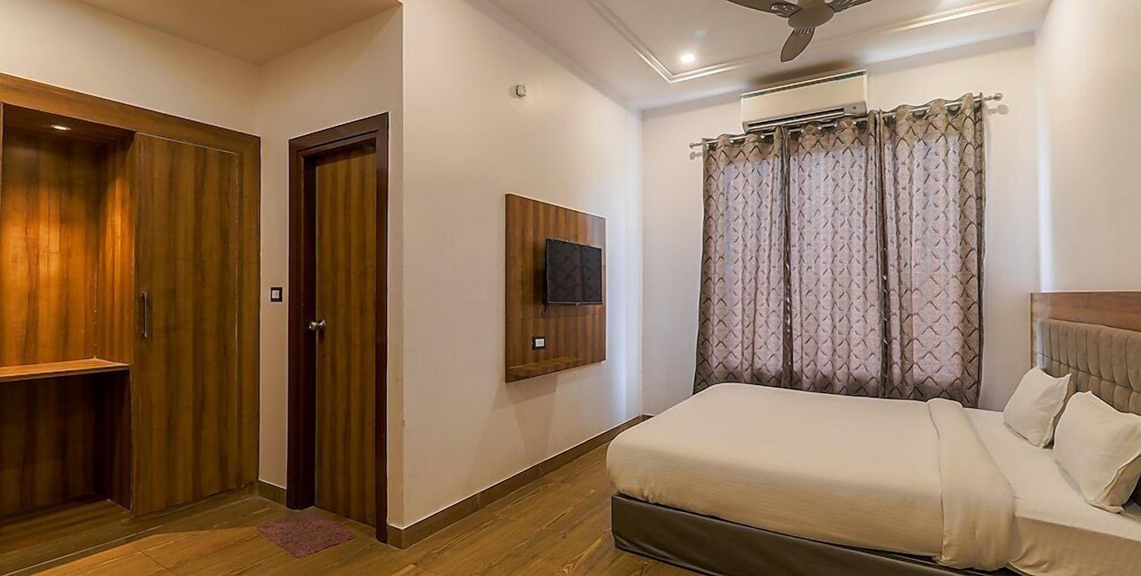 A bedroom with a bed, wooden wardrobe, a television on the wall, and a ceiling fan.