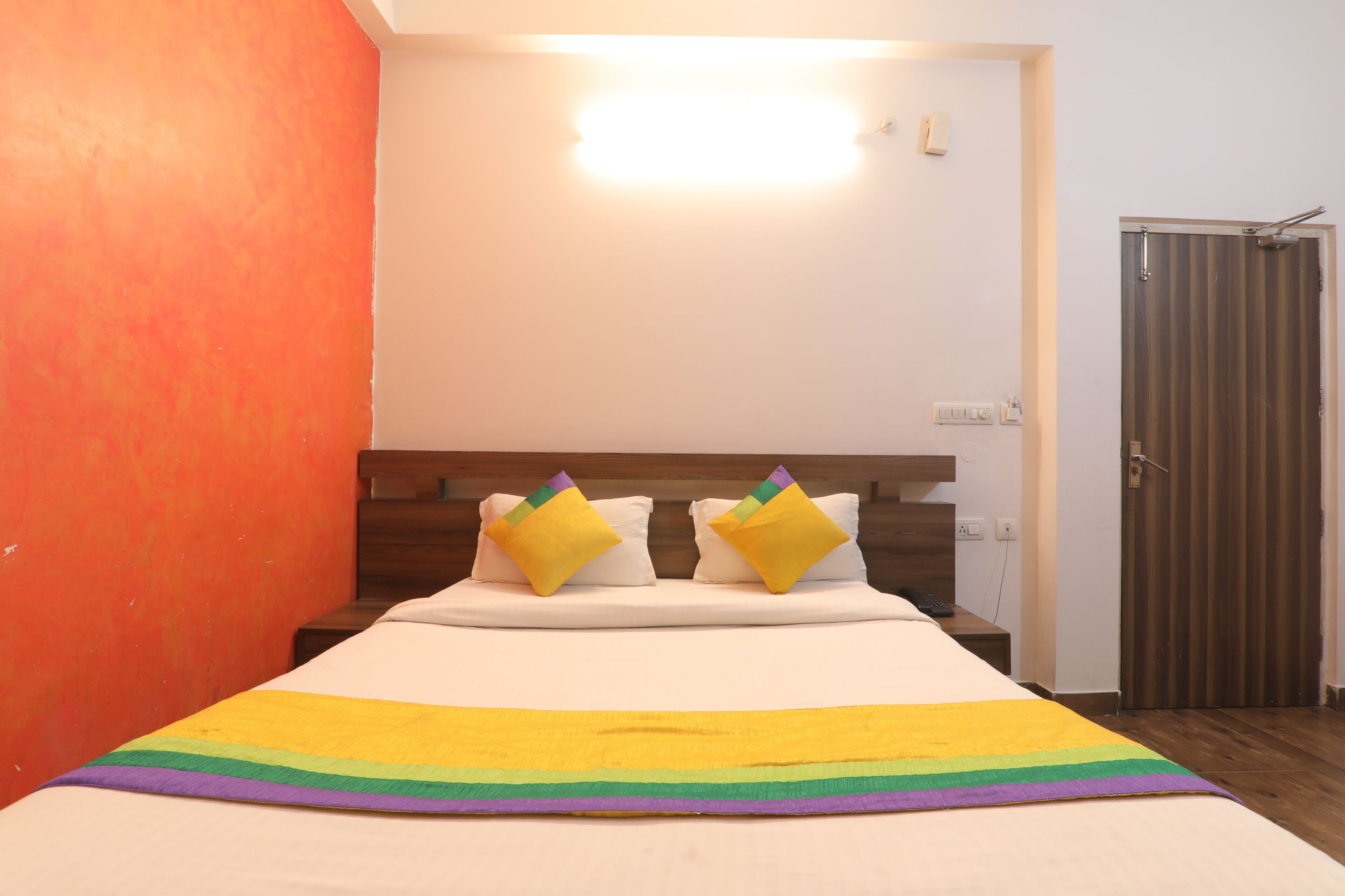 A hotel room with a bed, a nightstand, a wooden headboard, and a door.