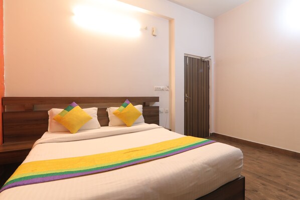 Una cama bien tendida con un edredón de rayas de arcoíris y dos almohadas, un cabecero de madera, una puerta cerrada y un interruptor de luz en la pared.
