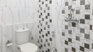Un baño con baldosas de mármol blanco, un inodoro blanco y una zona de ducha con pared revestida de azulejos.
