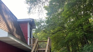 Un escalier en bois mène à une terrasse, qui est entourée d’une clôture blanche en piquets et d’un bâtiment rouge.