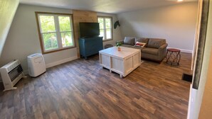 Une pièce avec un plancher en bois, une commode bleue, un canapé gris, une table basse blanche et un téléviseur fixé au mur.