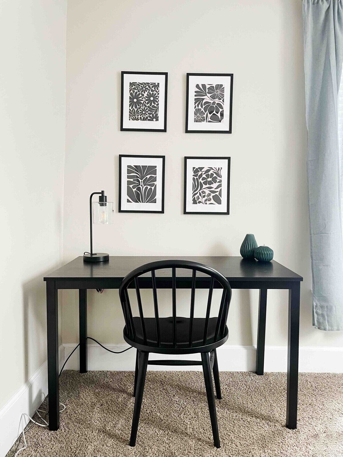 Une pièce comprenant un bureau noir, une chaise noire et quatre œuvres d’art encadrées en noir et blanc, accrochées au mur.