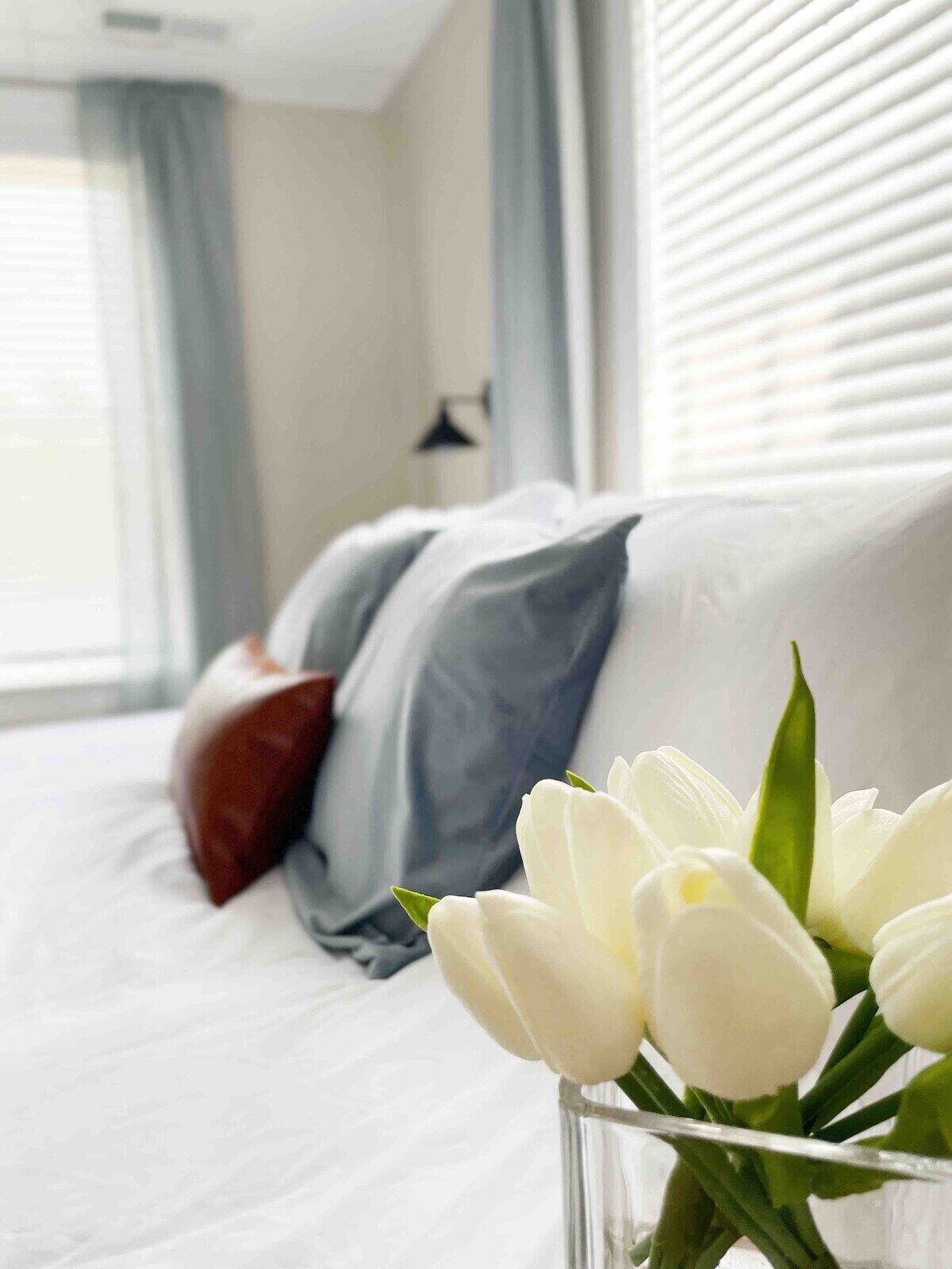 Habitación de hotel con una cama, un jarrón de flores blancas y una ventana con cortinas.