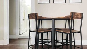 A dining area with a wooden table and four chairs, a white door, and three framed artworks on the wall.