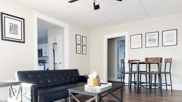 A modern living room with a black leather sofa, a coffee table, and a dining area with wooden chairs and a table.