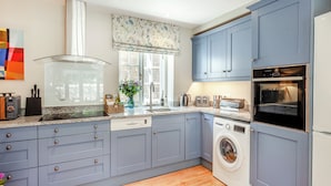 A modern kitchen with grey cabinets, a built-in oven, a washing machine, and a window with a floral curtain.