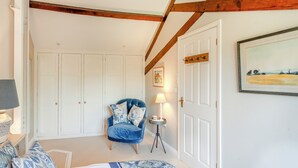 A bedroom with a bed, a chair, a lamp, a door, and a painting on the wall.