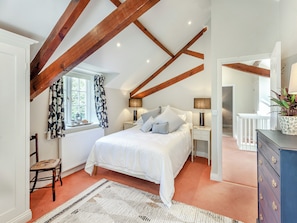 A bedroom with a bed, nightstands, a dresser, a window with curtains, and exposed wooden beams.