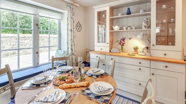 A dining area with a table set for four, a window with curtains, and a cabinet with glass doors.