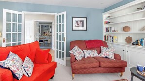 A living room with two red sofas, a bookshelf, and a door leading to a kitchen.