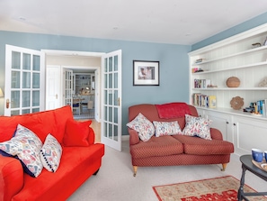 A living room with two red sofas, a bookshelf, and a door leading to a kitchen.