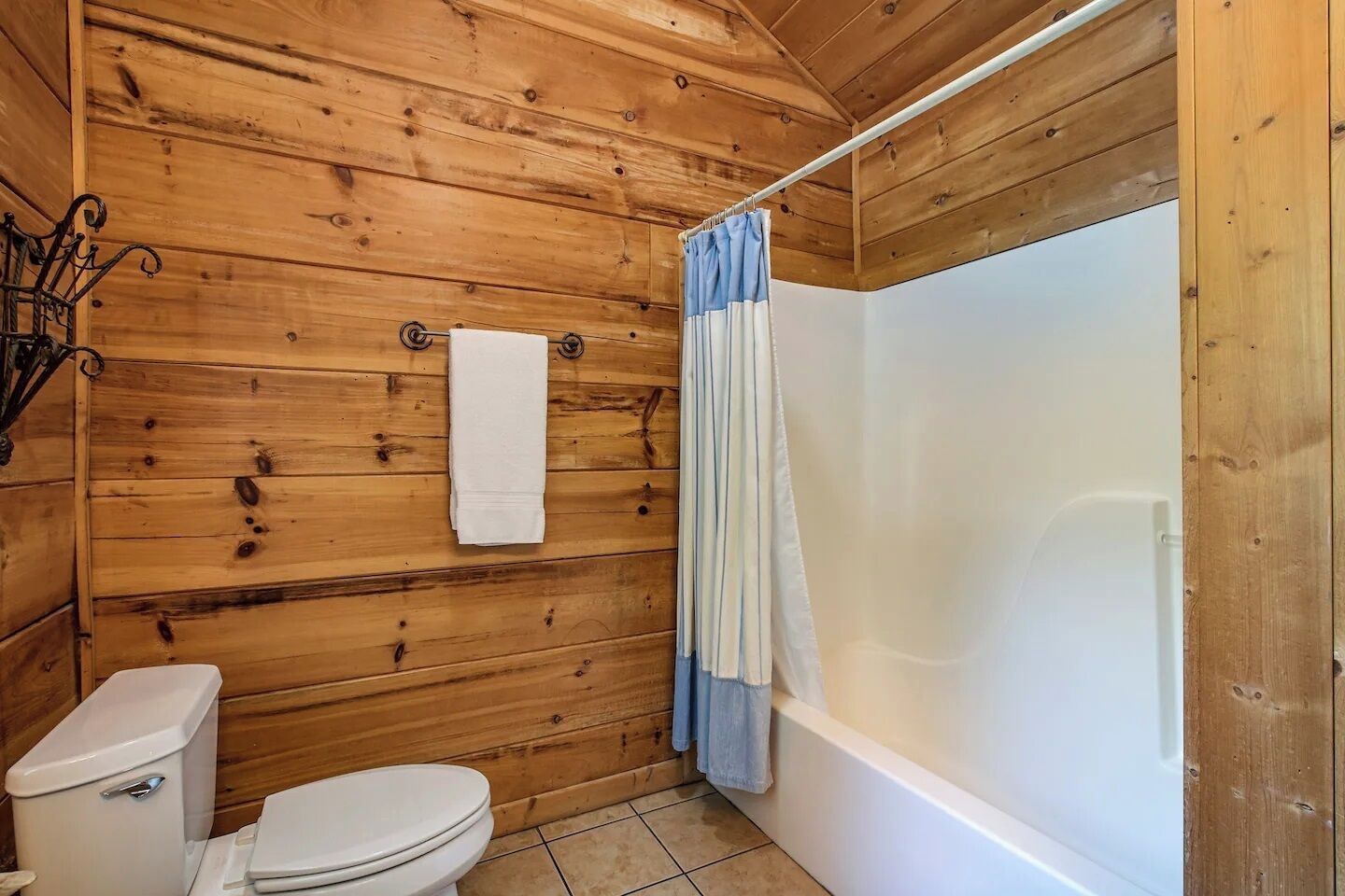 Baño de cabaña de madera con inodoro, bañera y cortina de ducha.