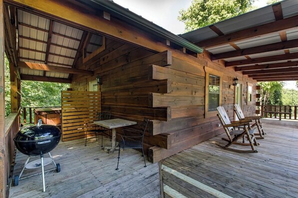 Una cabaña de madera con porche cubierto, una parrilla y mobiliario para exterior.
