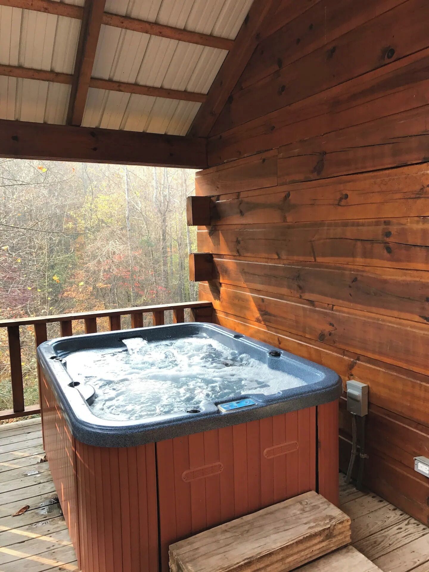 Ein Whirlpool auf einer Holzterrasse mit einer Holzhüttenwand im Hintergrund.