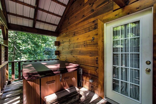 A wooden cabin with a porch, a hot tub, and a door with a window.