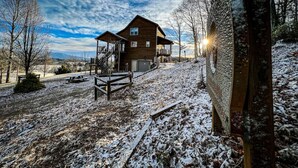 Une cabane en bois dotée d’un porche et d’un escalier menant à l’entrée, entourée d’un paysage enneigé.