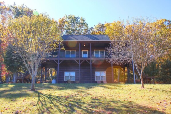 A two-story log cabin with a balcony, surrounded by trees with autumn foliage.