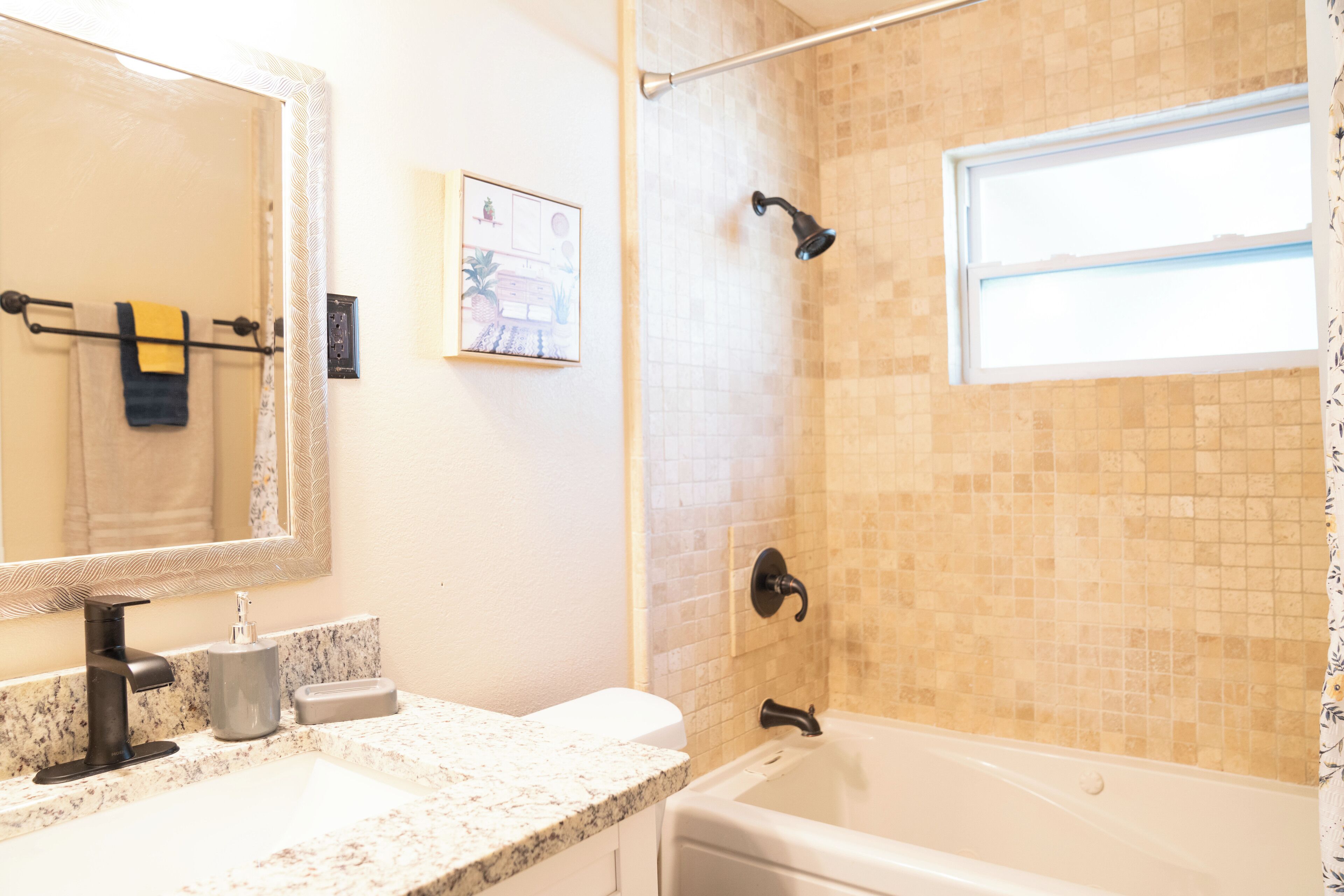 A bathroom with a sink, mirror, towel rack, shower, and a window.