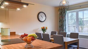 A modern kitchen with a wooden countertop, a fruit bowl, a clock, and a dining area with chairs and a table. - 3 bedroom accommodation in Helmsley (Helmsley)