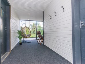 Un pasillo con alfombra gris, una silla colgante, una silla de madera y una planta en maceta.
