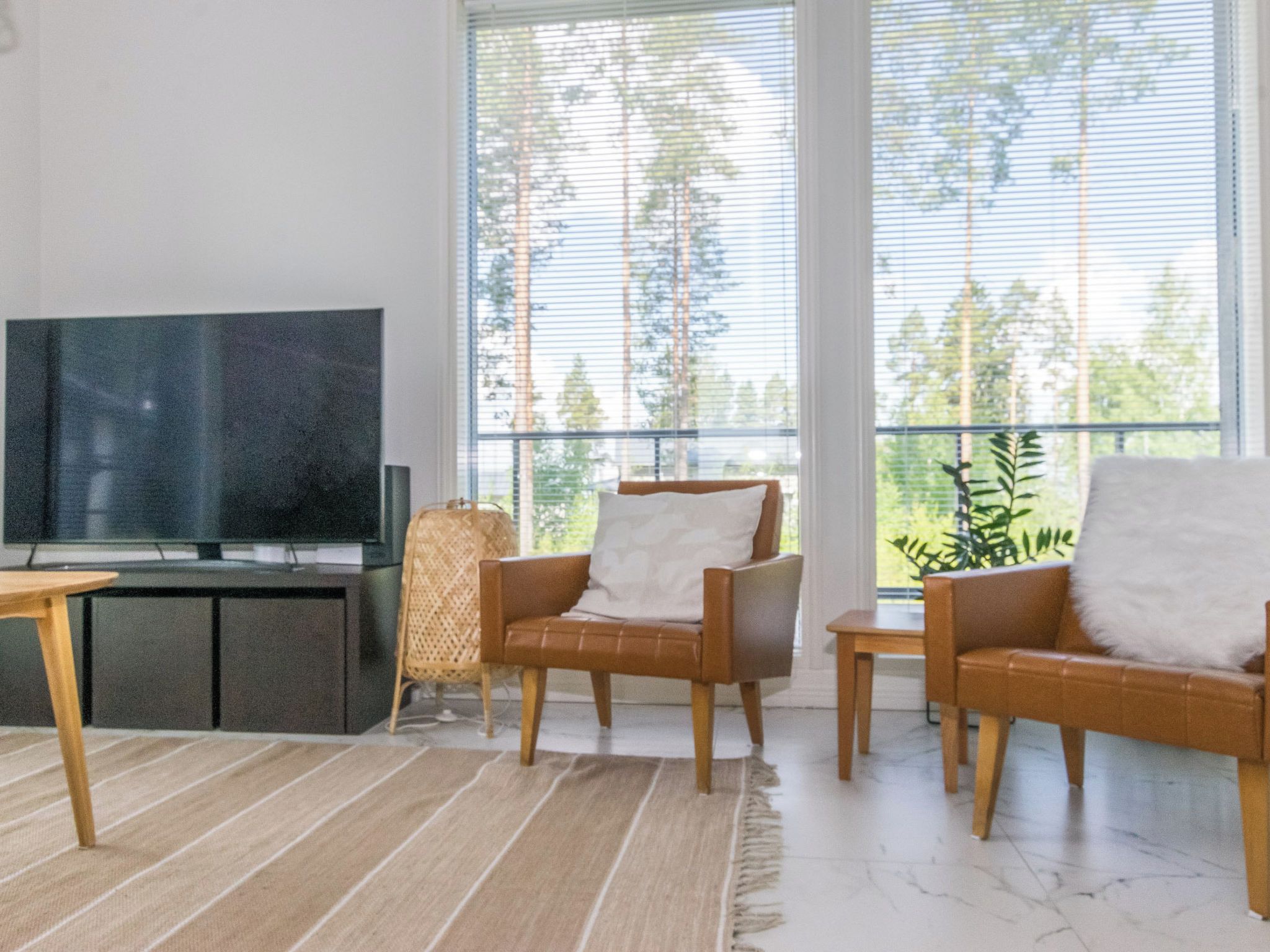 A living room with a flat-screen TV, two leather armchairs, a woven chair, and a large window with a view of trees.