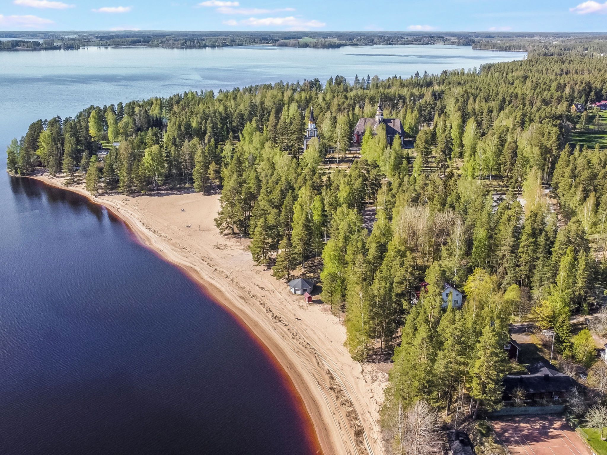 Una propiedad junto al lago con playa de arena, bosque denso y varias cabañas.