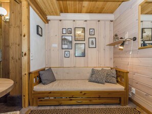 A wooden interior with a sofa, wall-mounted pictures, and a lamp.